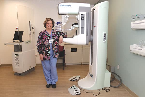 Friendly technician standing next to mammography machine