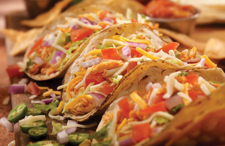 Three tacos with chicken, tomatoes, onions and cheese