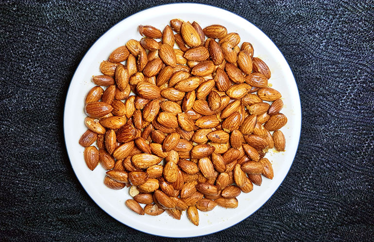 Fried and spiced almond nuts in white plate on dark background