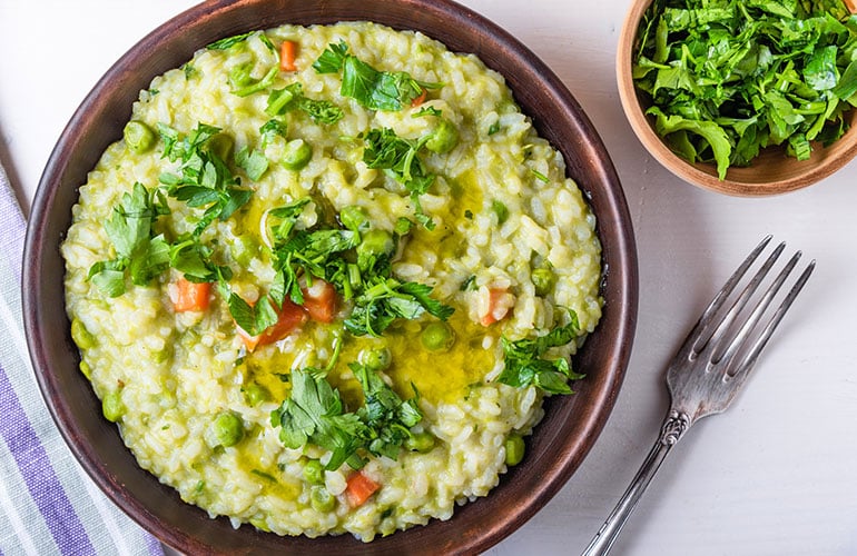 Traditional Italian vegetarian risotto with peas, carrots and parsley in rustic style, closeup 